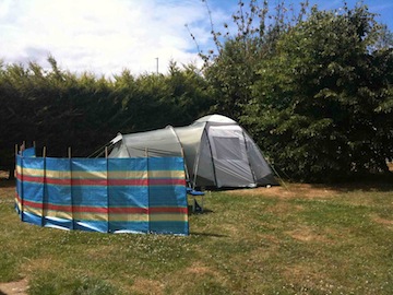A tent and a striped windbreak pitched in a corner of the field by the hedge